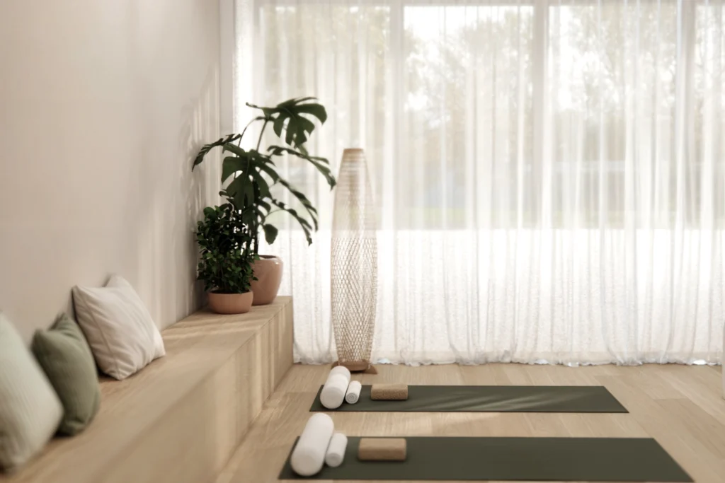 Svetel joga studio z lesenimi tlemi, vadbenimi blazinami, rastlinami in velikimi zavesami za sproščeno wellness izkušnjo. 